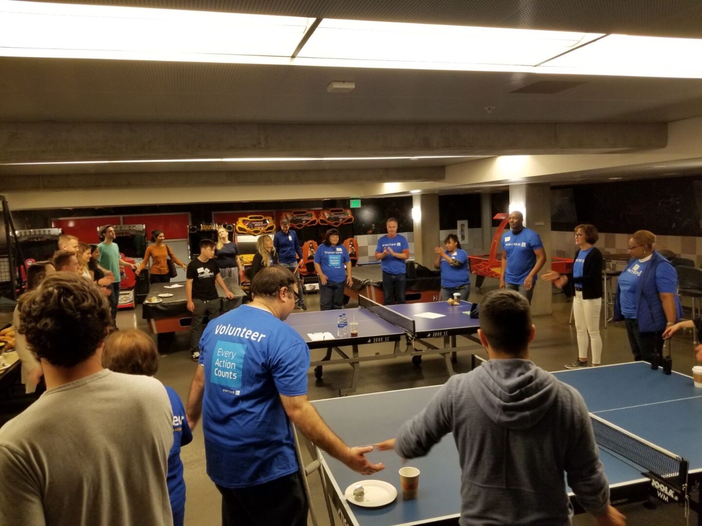 A group of people standing around ping pong tables.