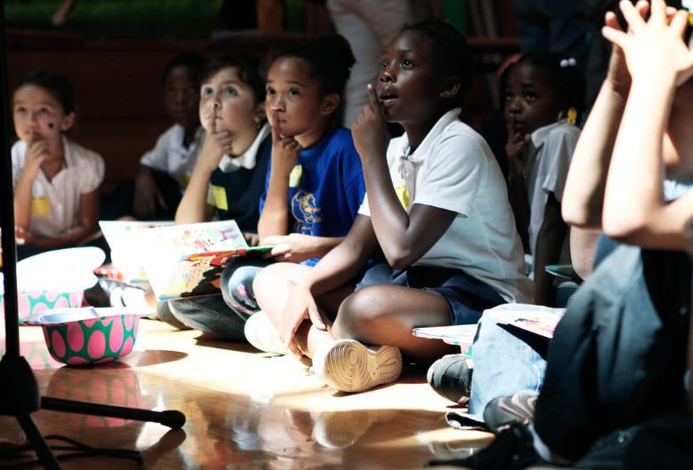 A group of kids sitting on the floor watching something.