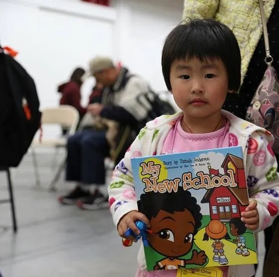 A little girl holding up a book in front of some people.